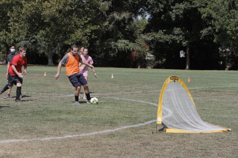 Dylan Samuel (orange jersey) shoots a ball at the goal, supported by volunteer Paige Beater.