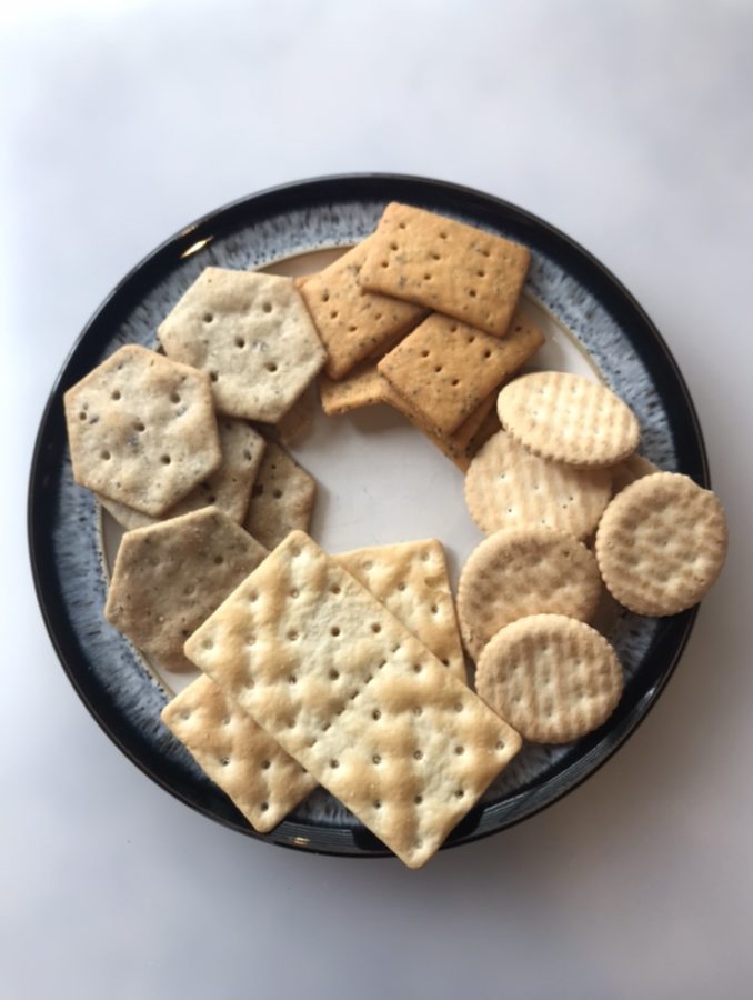 Starting at noon and moving clockwise, the crackers are as follows: Mary’s Gone Crackers Real Thin Sea Salt, Schär Entertainment Crackers, Schär Table Crackers and Simple Mills Organic Seed Flour Crackers.