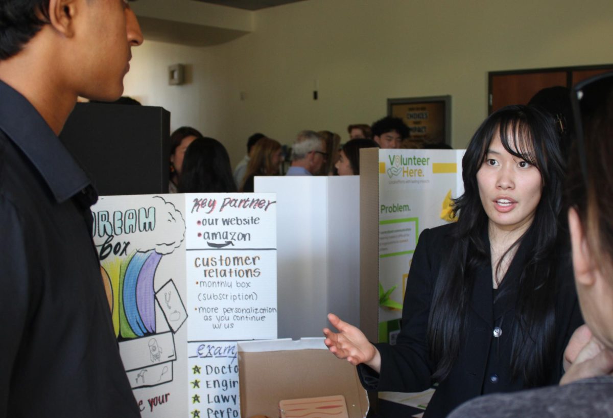 Leanna Change and Shaun Rays discuss their product to a visitor. Dream Box is a product for young kids to gain inspiration on a future career.